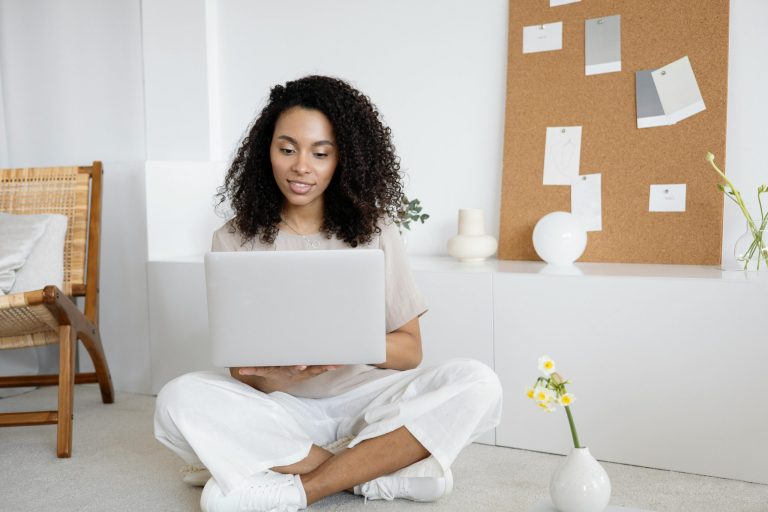 Young woman with curly hair working on her laptop in a cozy home setting, exuding confidence and focus.