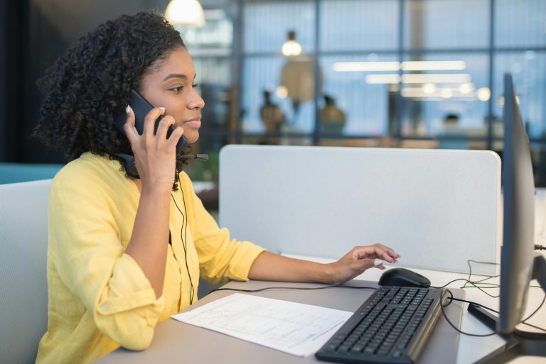 A young woman working in a modern call center environment, engaging in conversation via headset.